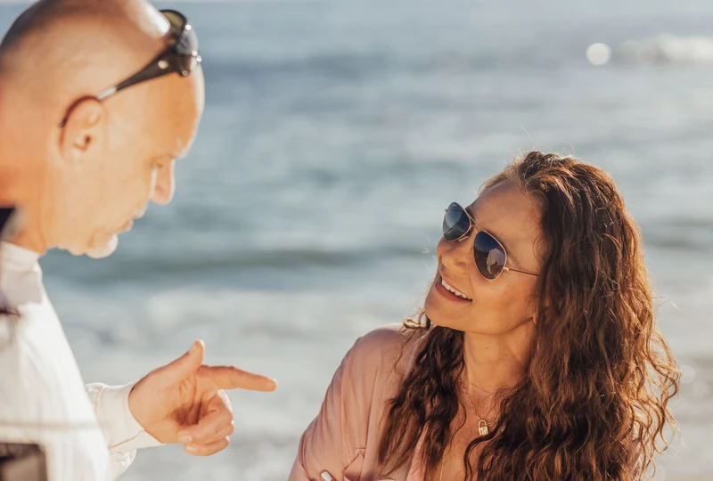 A man and a woman chat and smile together by the water on a sunny day
