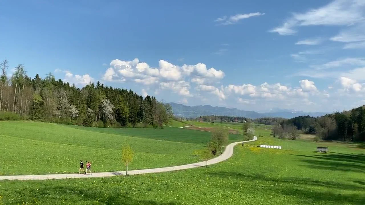 A winding path crosses green countryside under a bright blue sky with white clouds